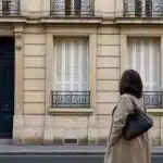 Personne vue de dos devant façade beige aux volets fermés